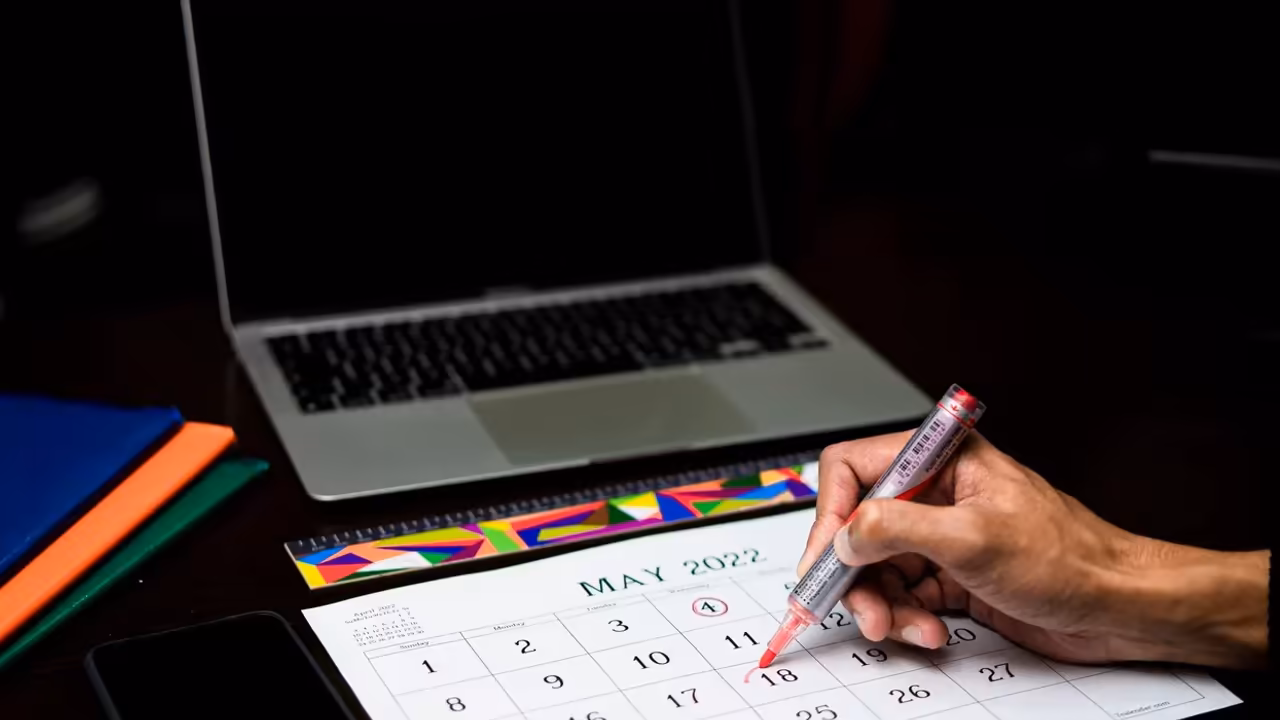 Osoba zaznaczająca termin w kalendarzu obok laptopa